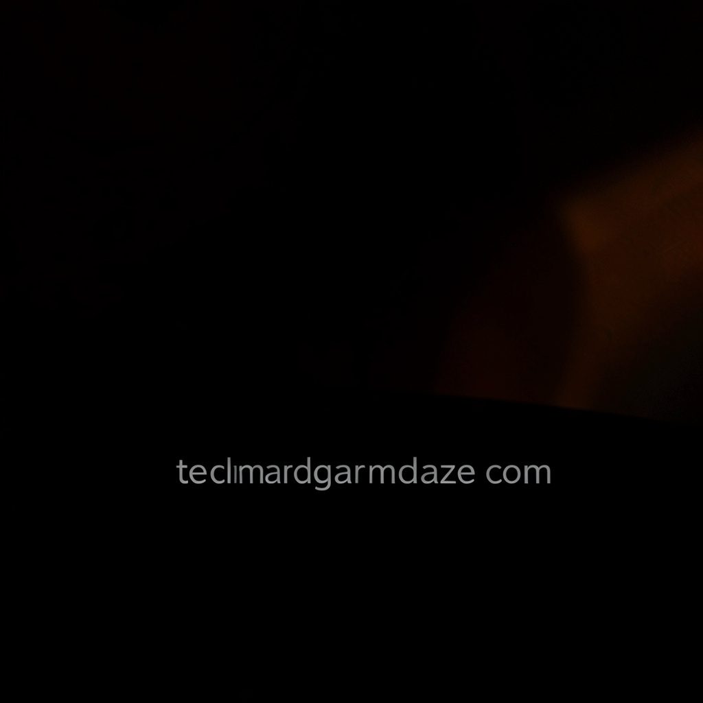 A dark, low-key photograph with deep shadow, featuring a moody desk setup with a glowing laptop screen, scattered notes, and warm ambient light spilling across the surface, conveying a late-night newsroom atmosphere.